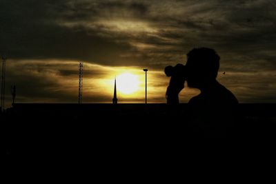 Silhouette man photographing against sky during sunset
