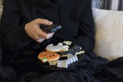 Midsection of woman on sofa with tv remote and halloween cookies