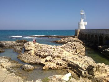 Tower by sea against clear sky on sunny day