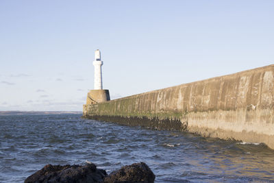 Lighthouse by sea against clear sky