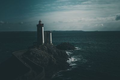 Lighthouse amidst sea and buildings against sky