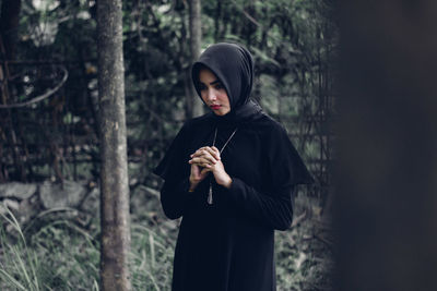 Young woman standing by tree in forest