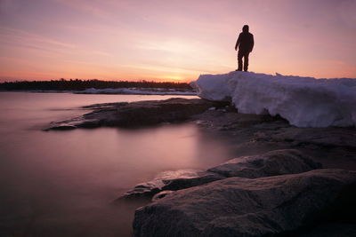 Rear view of man standing on rock at sunset