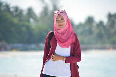 Smiling young beautiful woman wearing pink hijab standing at beach