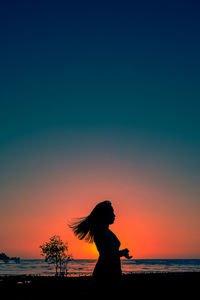 Silhouette woman on beach against sky during sunset