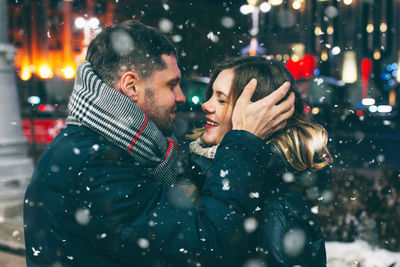 Couple romancing while standing against sky at night during snowing