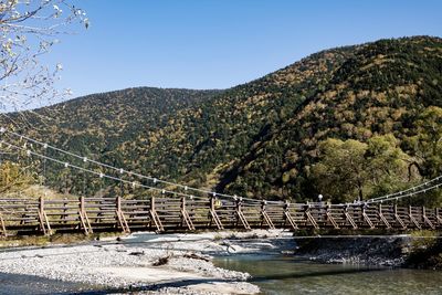 Bridge over river by mountains against clear sky