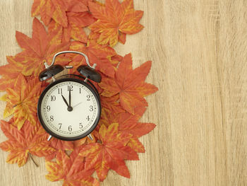Close-up of alarm clock with autumn leaves on table 