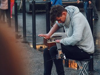 Full length of young man sitting on seat in street