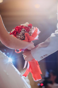 Cropped hands of bride and bridegroom holding bouquet during wedding ceremony