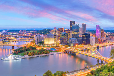 Illuminated buildings by river against sky in city