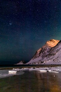 Scenic view of sea by snowcapped mountains against star field at night