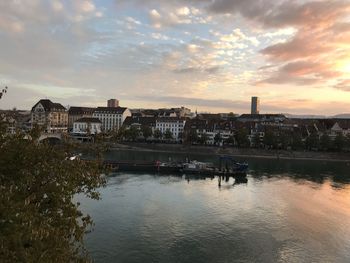 Buildings by river against sky during sunset