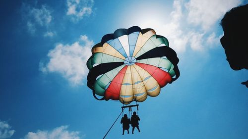 Low angle view of silhouette people enjoying paragliding against sky