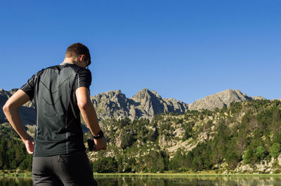 Rear view of man standing on mountain against clear blue sky