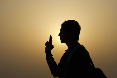 Silhouette man smoking cigarette against sky during sunset