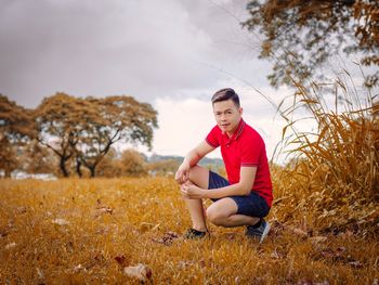 Young man sitting on field against sky