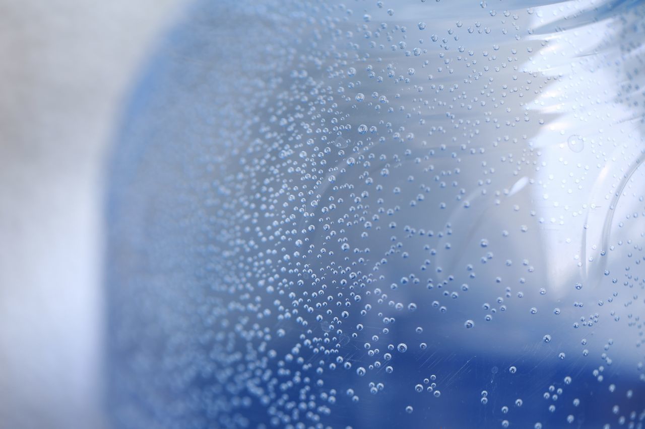 CLOSE-UP OF WET GLASS AGAINST BLUE WATER