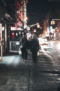 Rear view of people walking on illuminated street at night