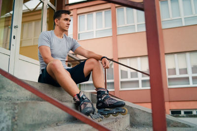 Man looking away while sitting on staircase against building