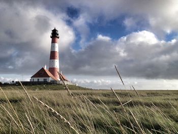 Lighthouse on field against cloudy sky