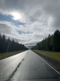 Empty road along trees and against sky