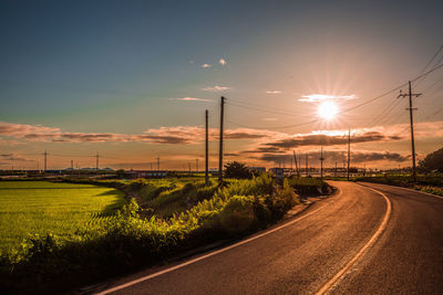 Road by trees against sky during sunset
