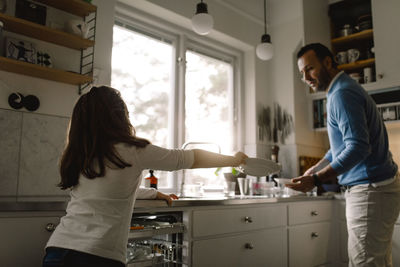 Daughter giving plate to father while standing in kitchen at home