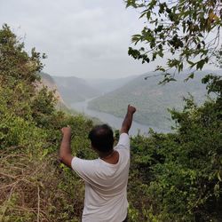 Rear view of man standing on mountain against sky