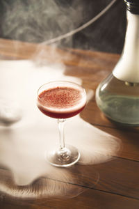 Close-up of coctail in glass on table with hookah smoke