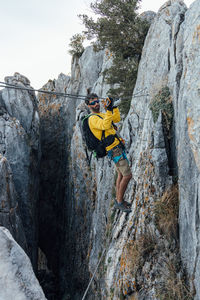 Full body side view of male mountaineer with backpack and safety equipment preparing to cross over rocky ravine on zipline while practicing extreme adventure in mountains