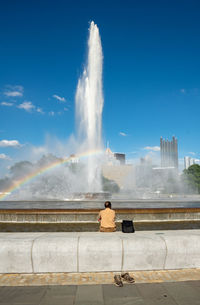 Rear view of man sitting on fountain against sky