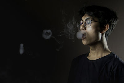 Portrait of young woman standing against black background