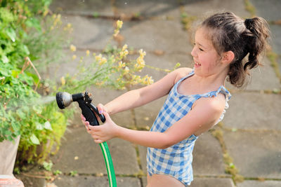 Young girl is watering plants in the backyard while wearing a bathing suit