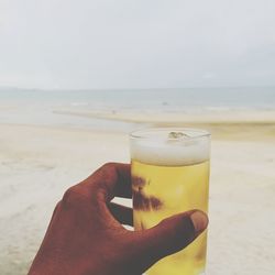 Cropped hand holding drink at beach