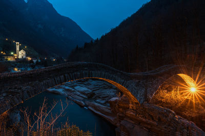 Illuminated bridge by mountains against sky at night