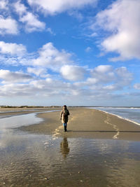 Rear view of woman walking at beach against sky