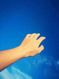 Cropped hand of woman against blue sky