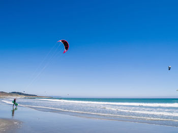 Person kiteboarding on shore against clear sky