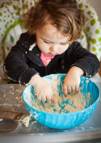 Close-up of baby girl holding dough in bowl on table at home