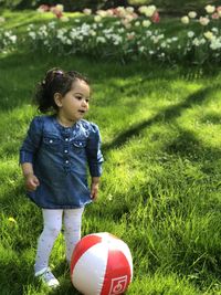 Cute girl standing by ball on field