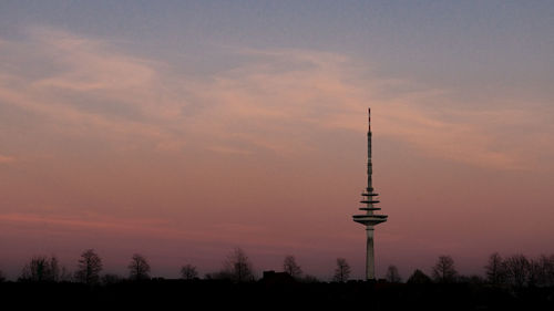 Silhouette of communications tower against cloudy sky