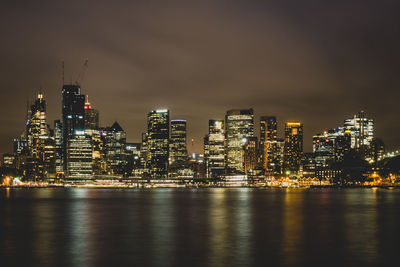 Illuminated buildings by river against sky in city at night