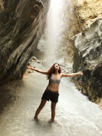 Full length of young woman standing against waterfall