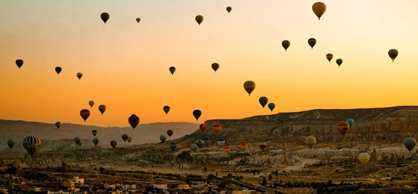 Hot air balloons flying over cappadocia against orange sky