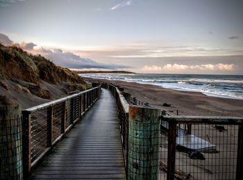 View of jetty on beach against cloudy sky