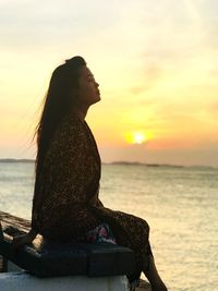 Woman sitting at beach against sky during sunset