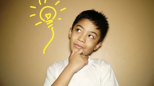 Thoughtful boy looking away while standing against wall
