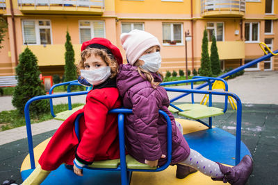 Rear view of siblings sitting on slide at playground