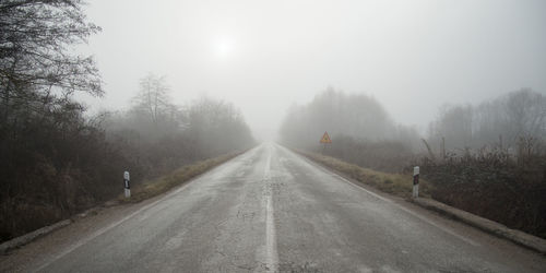 Empty road amidst trees against sky